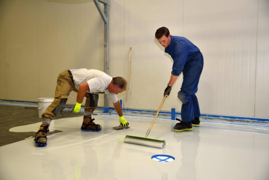 Dos empleados de Plancher Epoxy Sherbrooke aplican la capa de epoxi con una espátula y un rodillo.